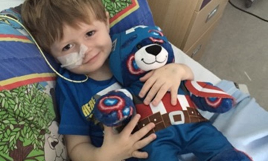 Two year old Cupar, who has a tube coming out his nose, smiles and cuddles a bear.
