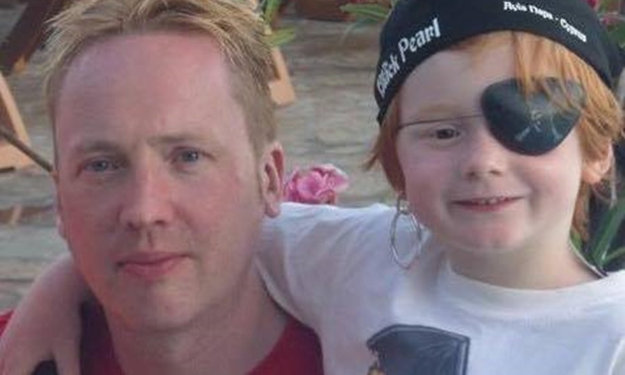 Allen on holiday with his son. The small boy wears a bandana and a patch, and has his arm round his dad's shoulder.