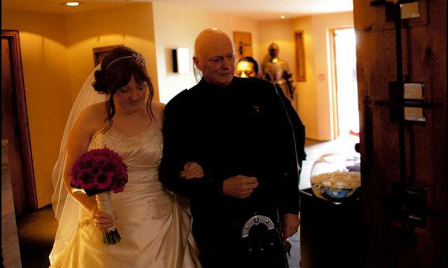 Jim, in his kilt, walks arm and arm with Louise, in her wedding dress. She is going to get married.