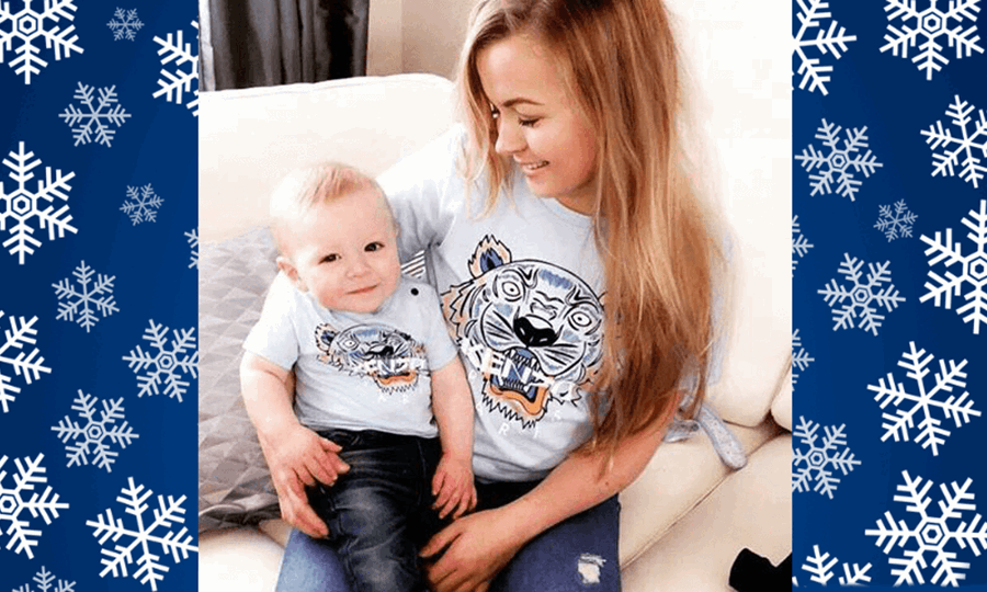 Rhiannon sits in living room with one year old Ollie on her knee. Both wear jeans and matching t-shirts.