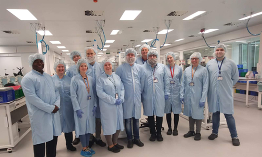 Biomedical science staff from Edinburgh pose for a group photo while wearing hair covers and overcoats. 
