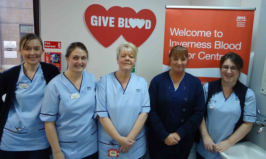 Nurses in uniform from Inverness Donor Centre pose for a photograph in front of a Give Blood sign. 