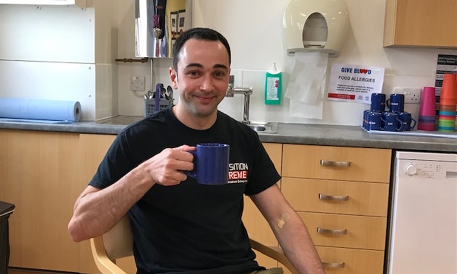 First time donor Sean holds up a cup of tea while smiling after giving blood. 