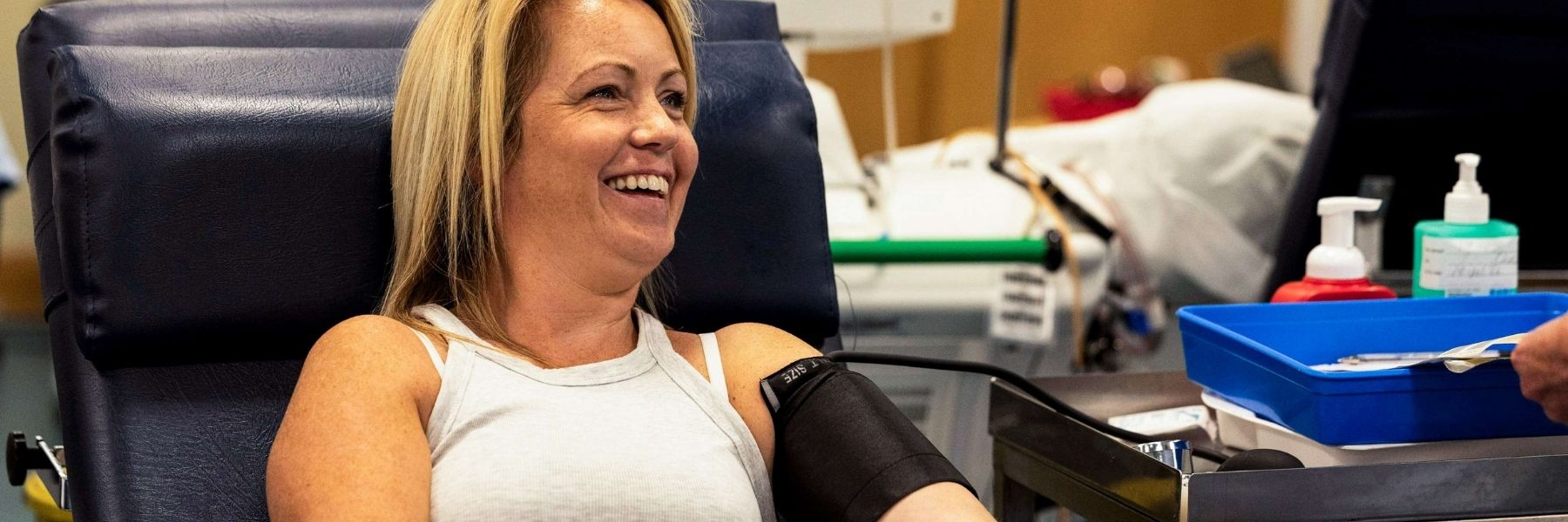Woman sitting in donation chair smiles while giving blood