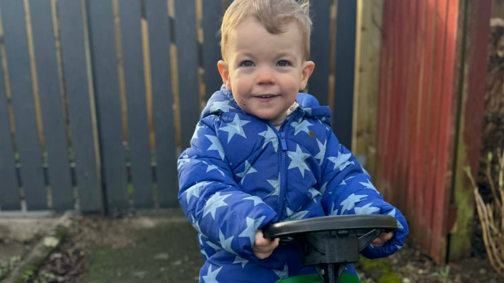 Harrison a small boy rides a toy tractor in his garden