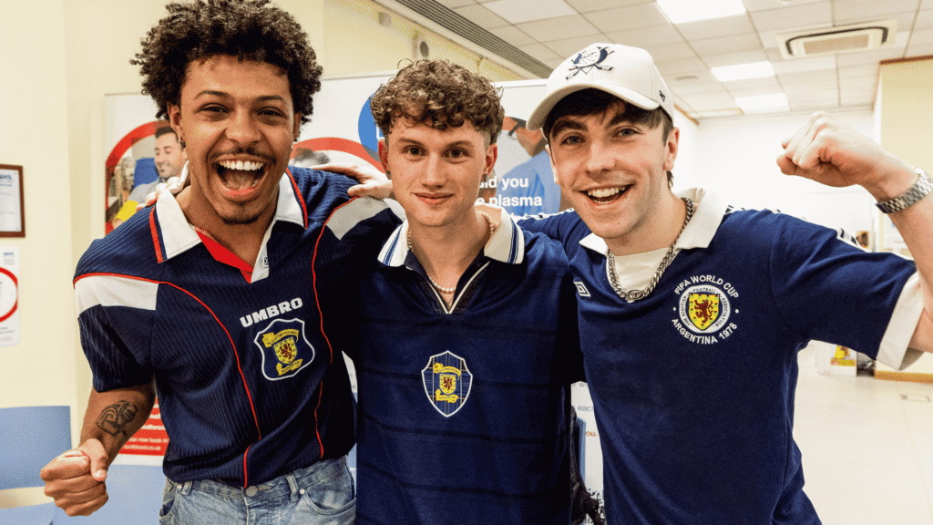 Three young men in scotland strips look cheerful in Glasgow donor centre