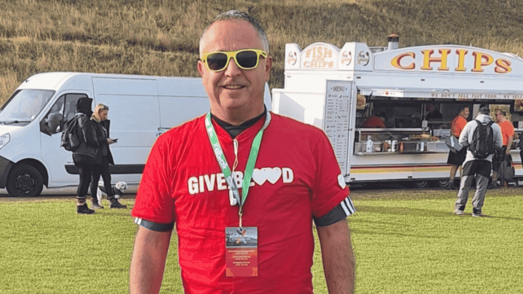 Pete wears a red Give Blood t-shirt and smiles at Arthur's Seat.Edinburgh o the day of the Kiltwalk