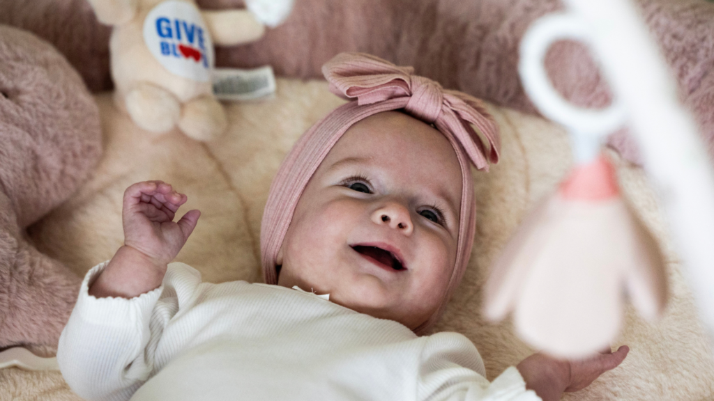 baby millie lies back in crib looking at toys and smiling